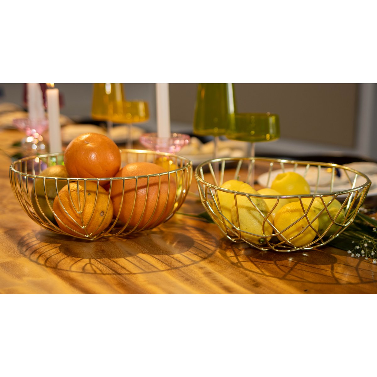 Two gold wire fruit bowls on a wooden table with oranges and lemons.