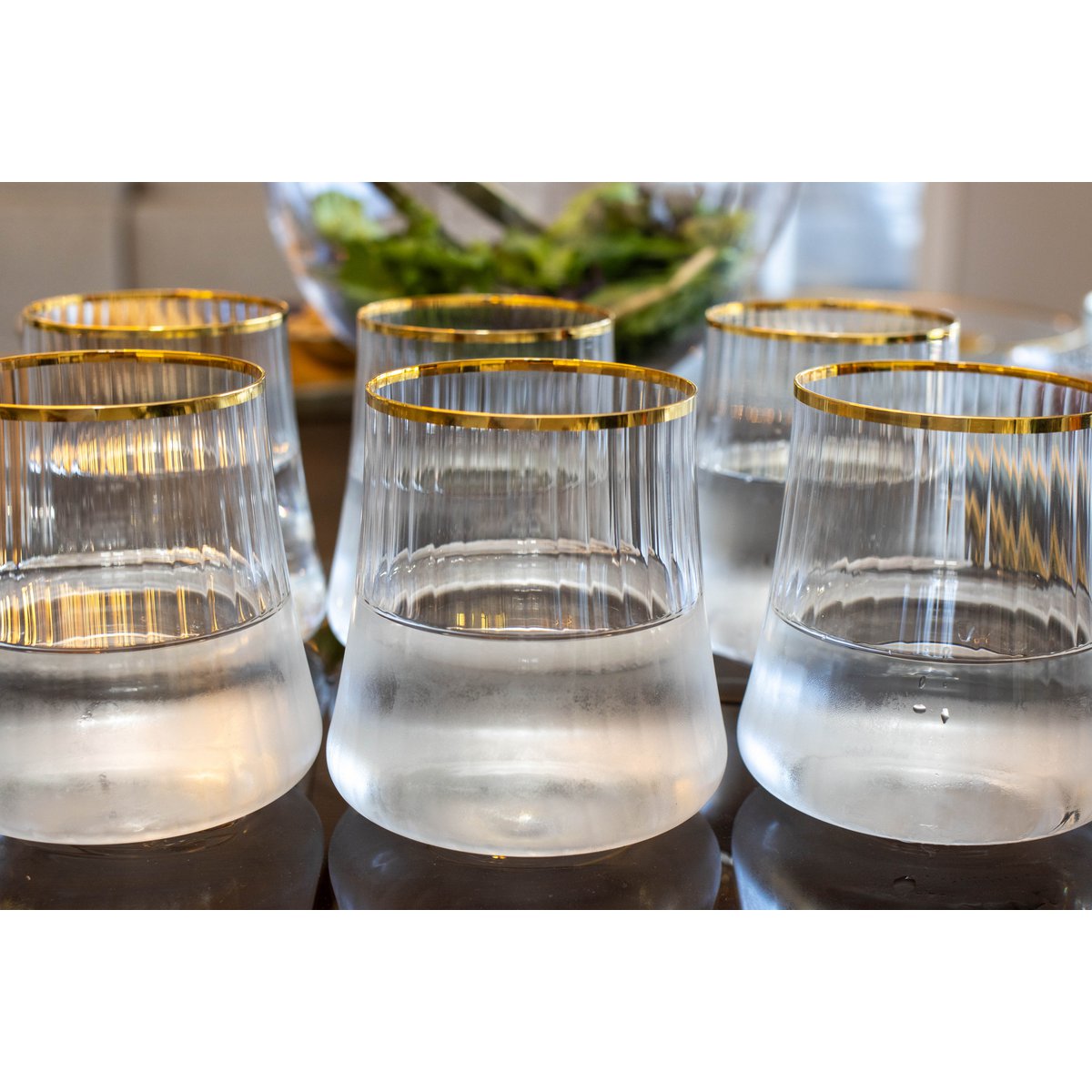 Set of clear glasses with gold rims on a reflective surface.