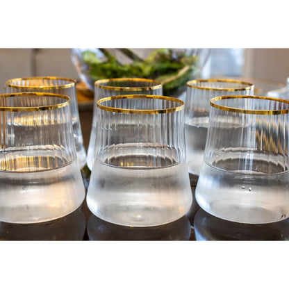 Set of clear glasses with gold rims on a reflective surface.