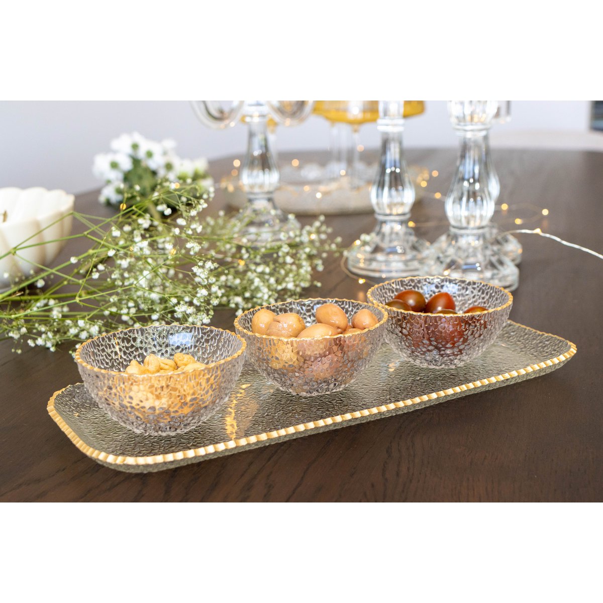 Decorative glass bowls with fruits on a tray with candles and flowers in the background