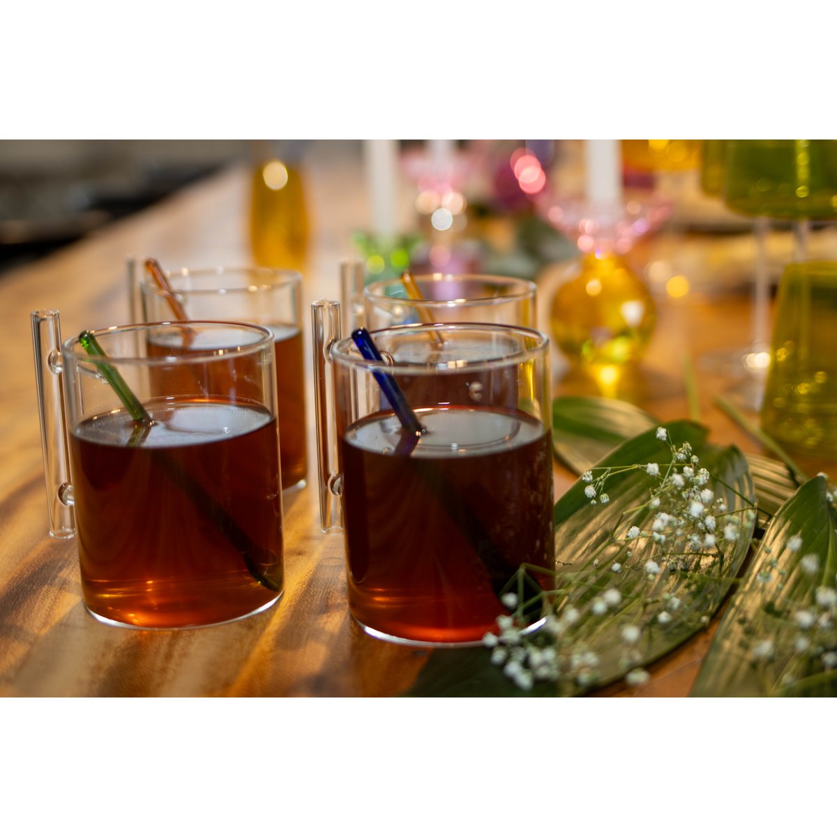 Glasses of amber liquid with straws on a wooden table with blurred lights in the background