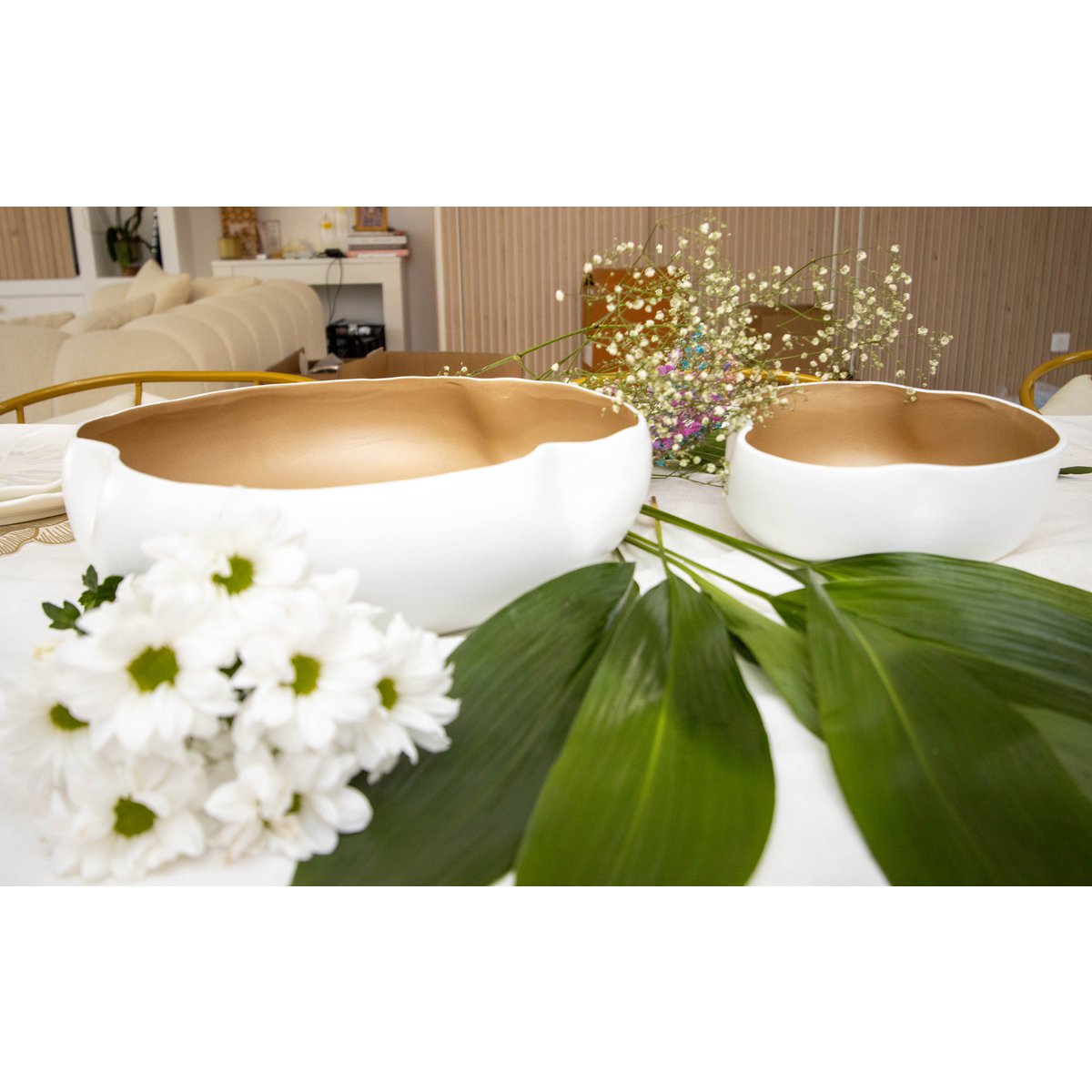 Two white bowls with gold interior on a table with flowers and leaves.