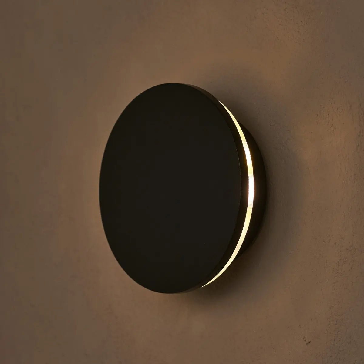 Round wall light fixture with black finish and gold rim on a brown wall.